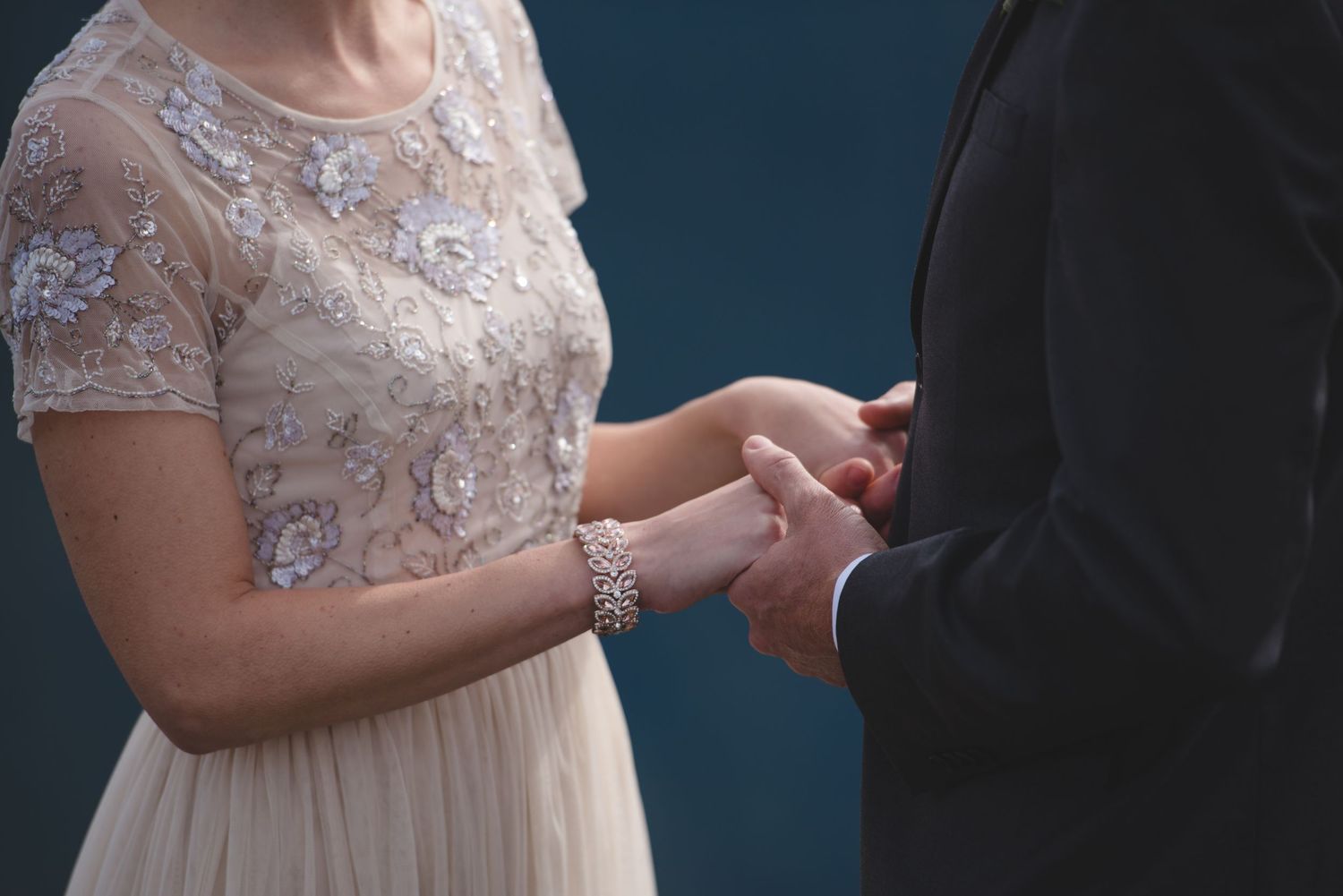 Close-up of couple holding hands during mountain-top wedding ceremony.