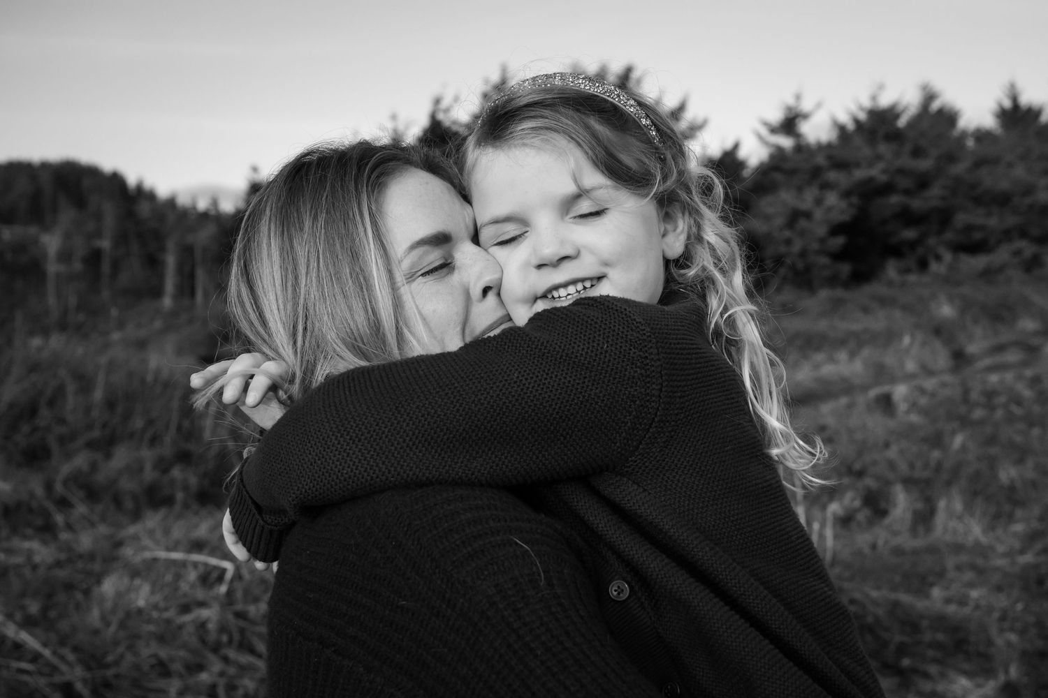 Black and white portrait showing an intimate embrace against a natural outdoor backdrop.
