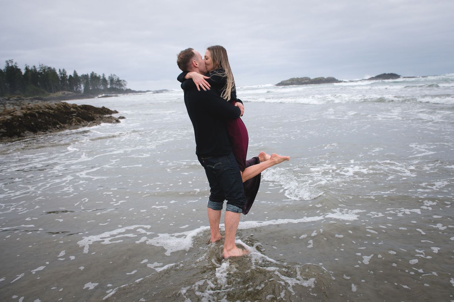 A romantic beach photoshoot with a couple embracing in the shallow ocean waves.