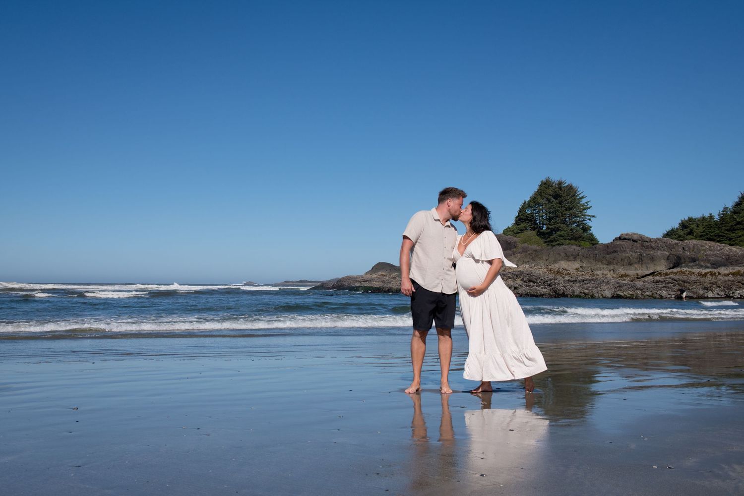 A couple embracing on a scenic beach with rocky cliffs in the background.