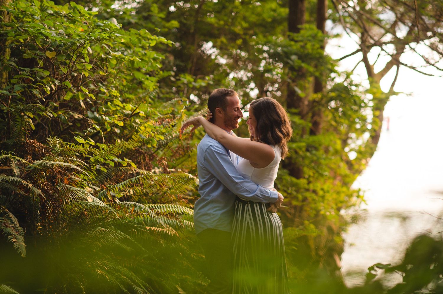 Romantic couple embraces in a lush forest setting during golden hour sunset.