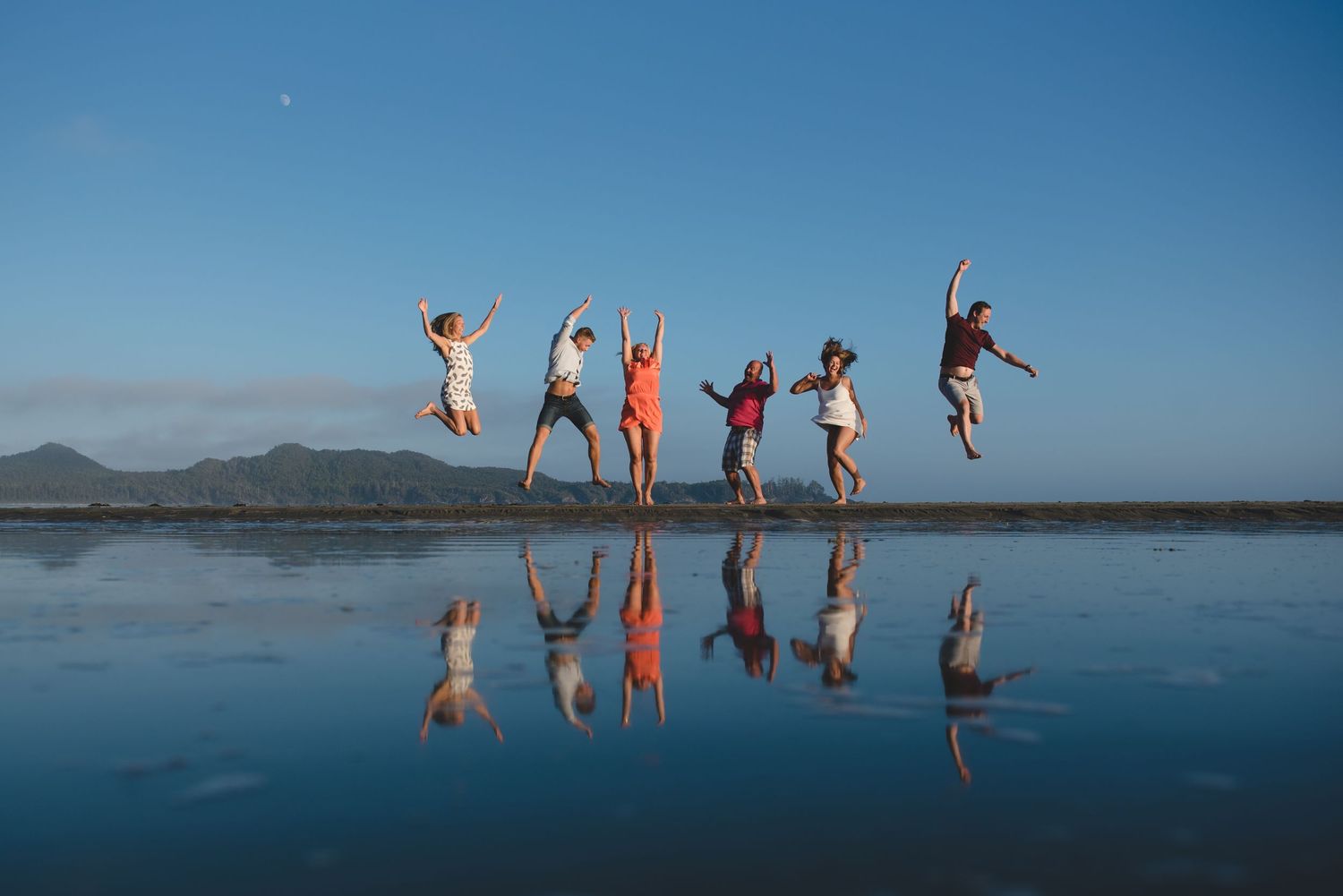 Silhouettes of people jumping joyfully against blue ocean horizon at sunset.