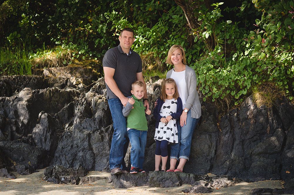 A group of people pose together along a stone wall surrounded by lush green foliage on a sunny day.