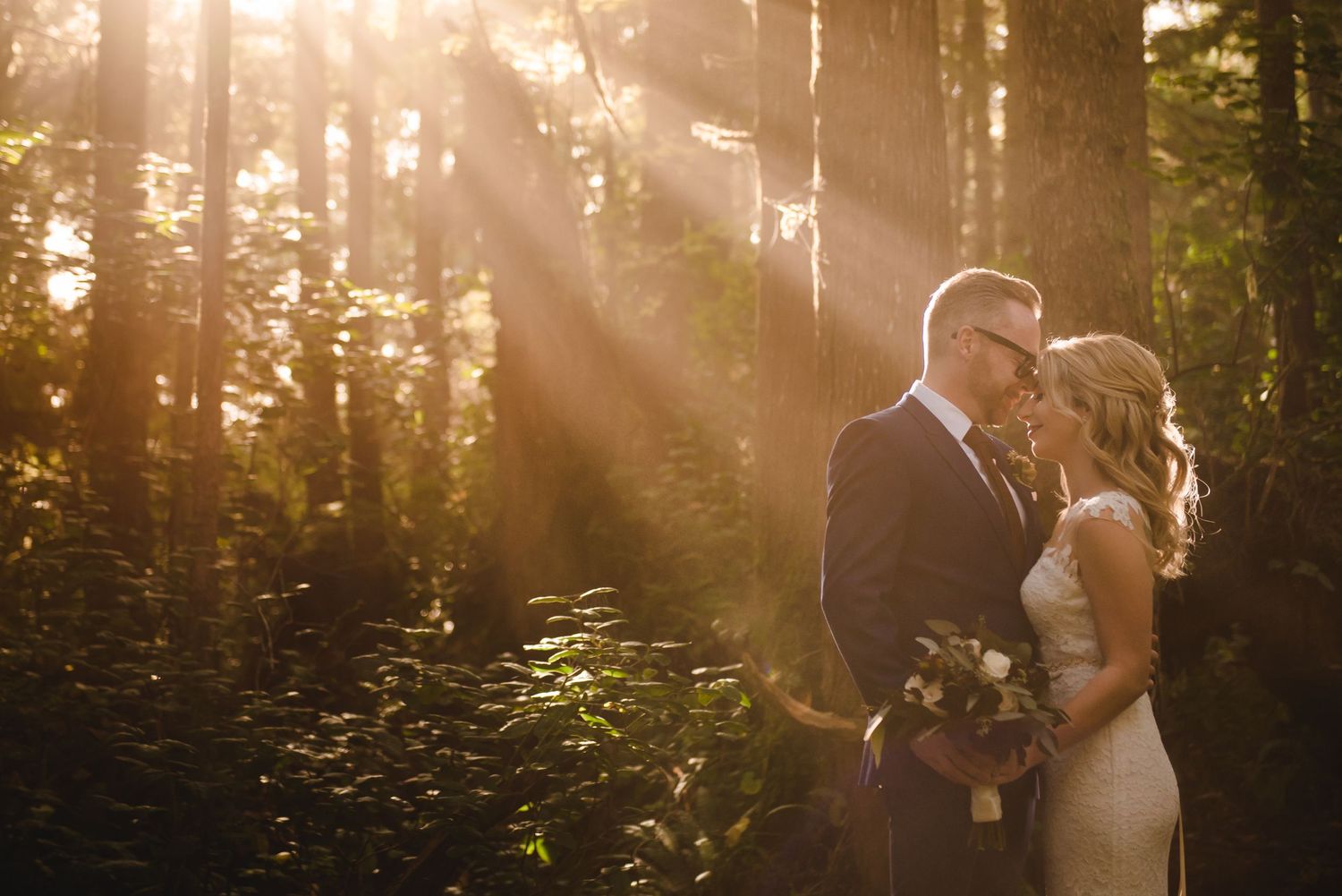A romantic wedding moment captured in a sunlit forest with rays streaming through the trees.