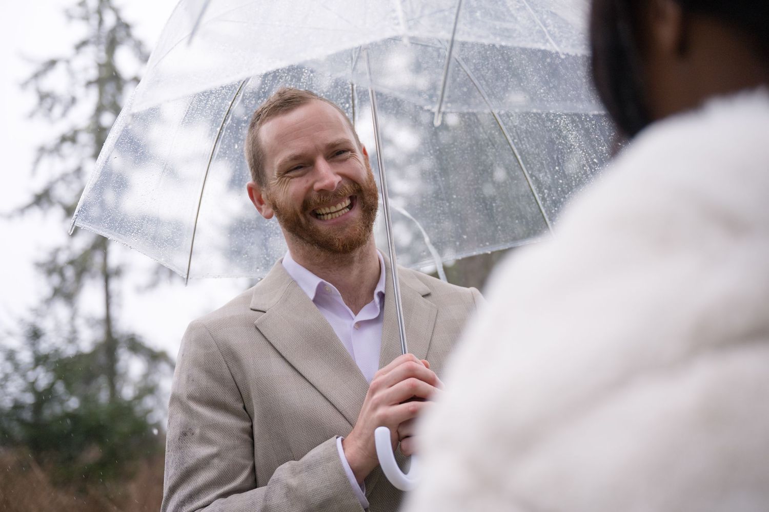 A joyful moment shared under a clear umbrella on a rainy wedding day.