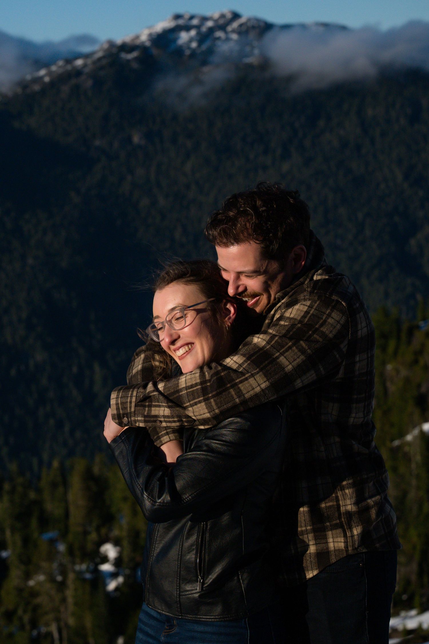 Happy couple embracing and laughing together against a stunning mountain backdrop in winter.