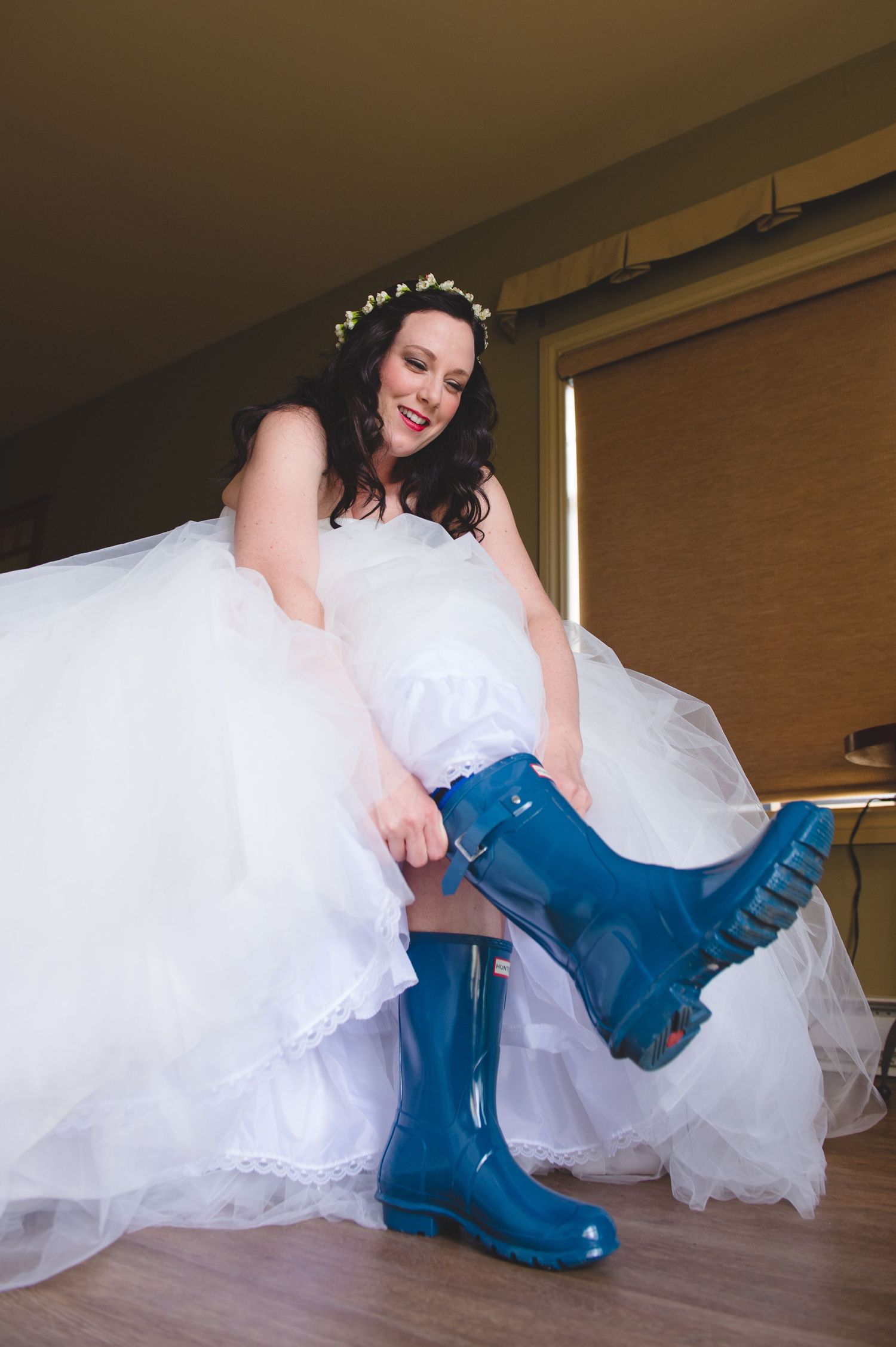 A bride wearing a white gown shows off bright blue rain boots beneath her dress.