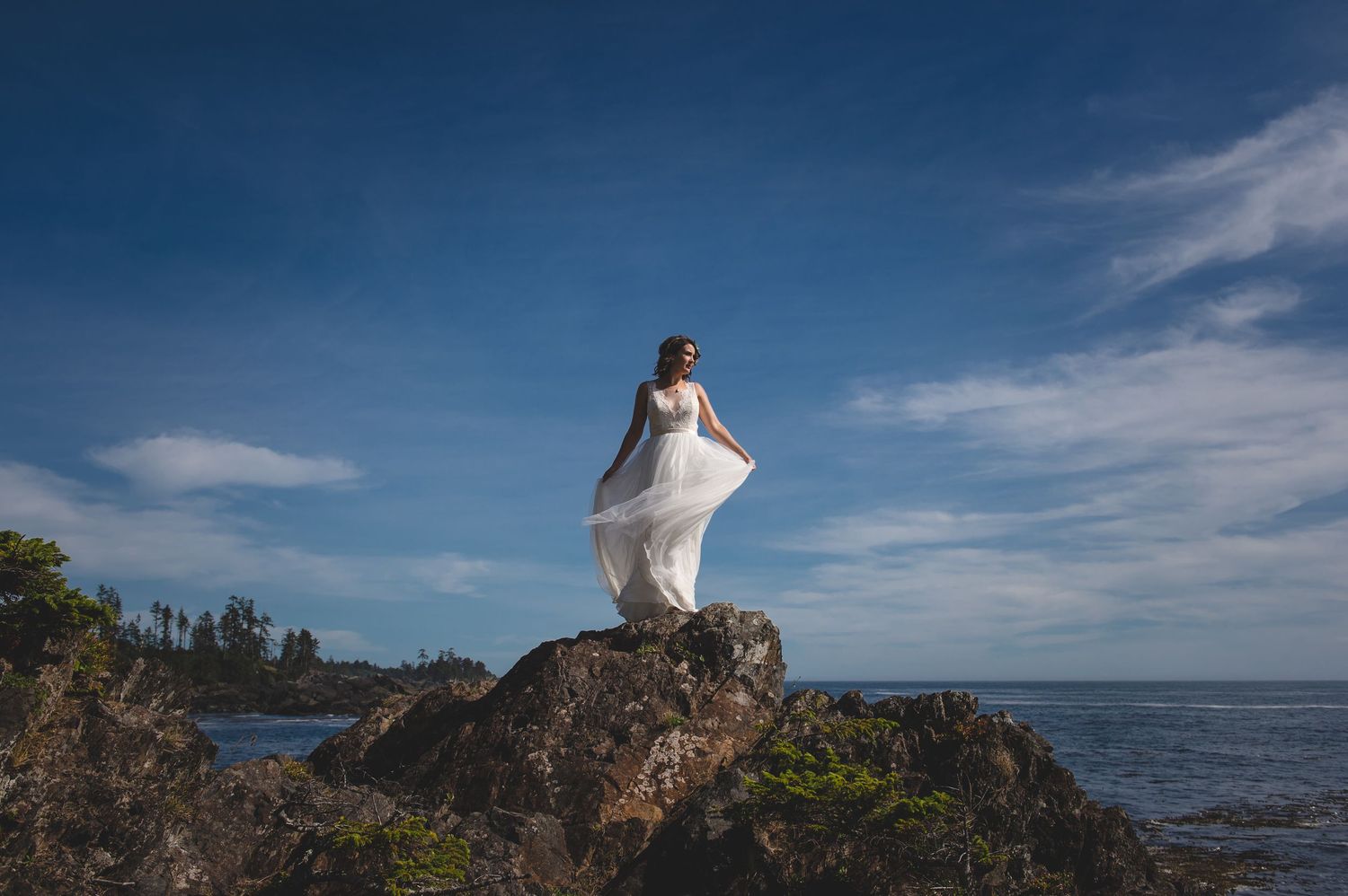 Dramatic coastal wedding photos with rocky cliffs and ocean waves under blue skies.