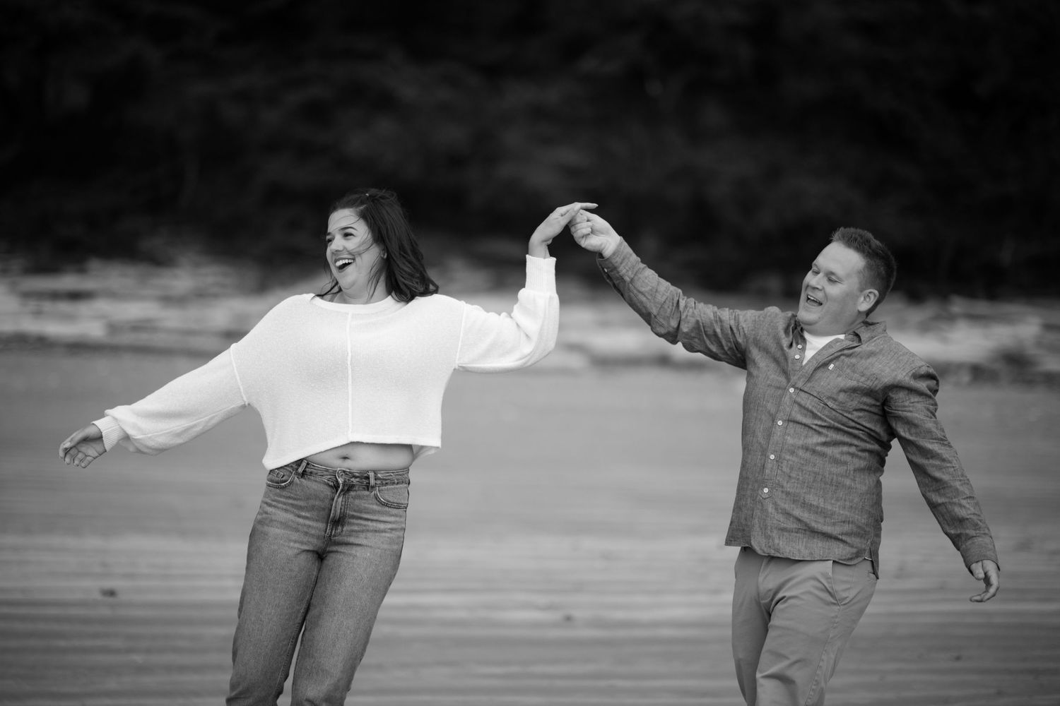 Black and white photo of a couple dancing joyfully in an outdoor setting.