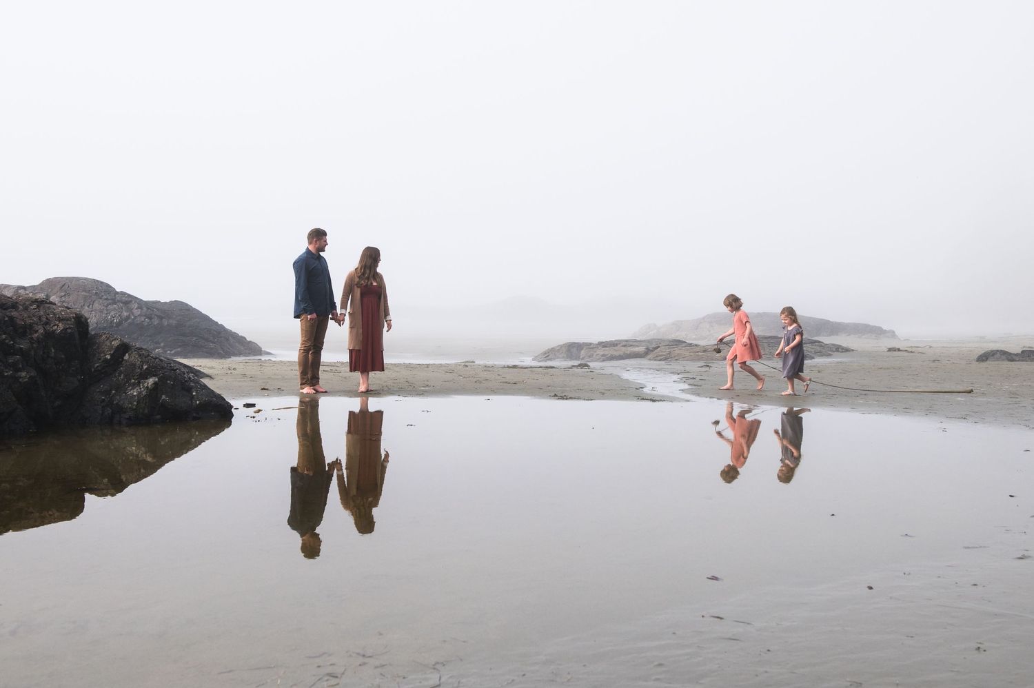 Group strolling on empty beach with dramatic coastal cliffs in background.