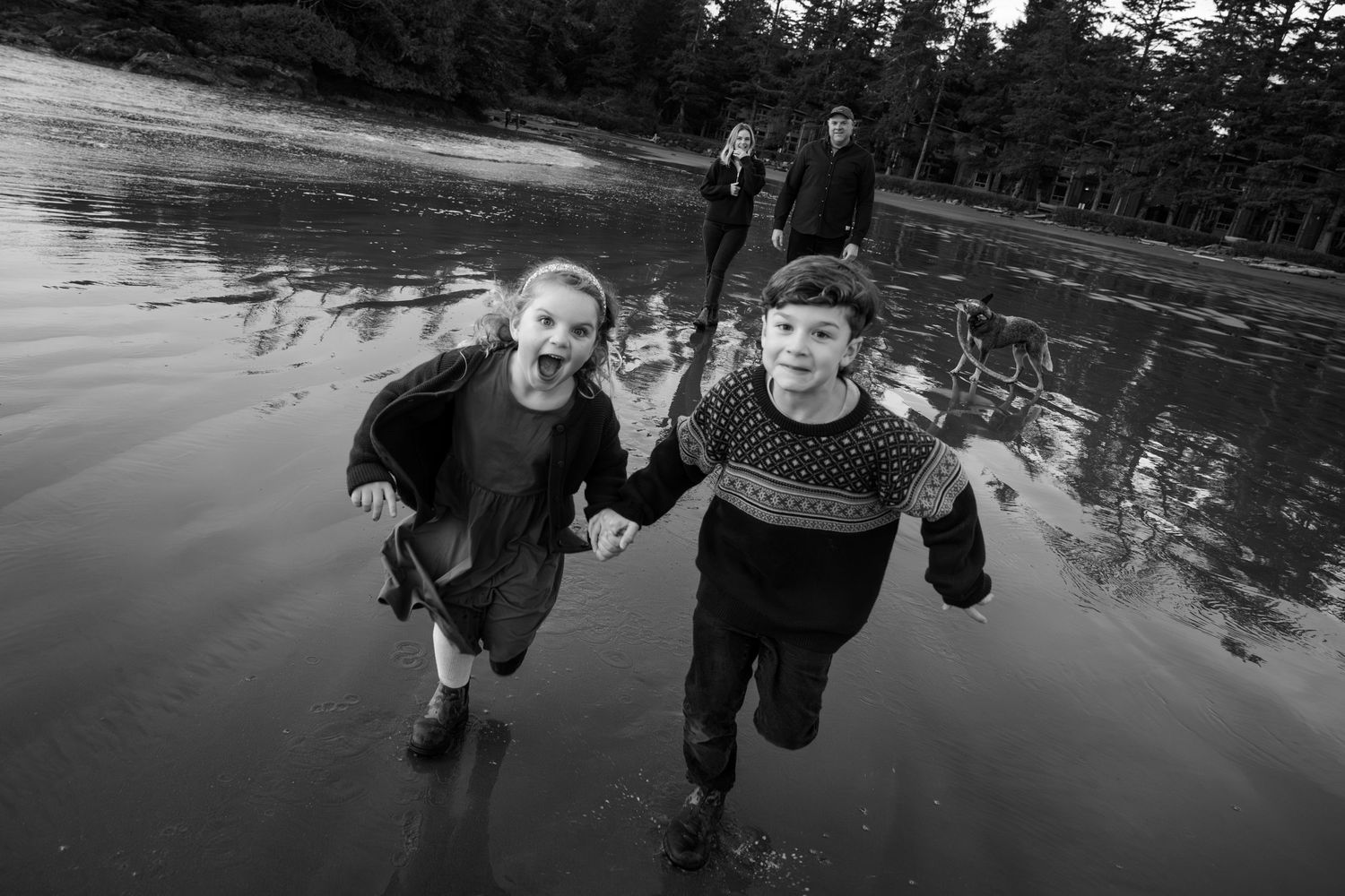 Black and white action shot of children running joyfully through shallow water.