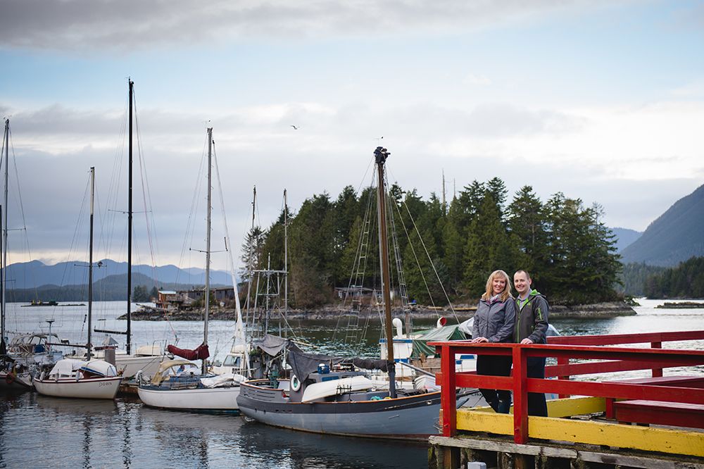 Marina filled with sailboats and vessels moored at a peaceful harbor surrounded by evergreen trees and mountains.