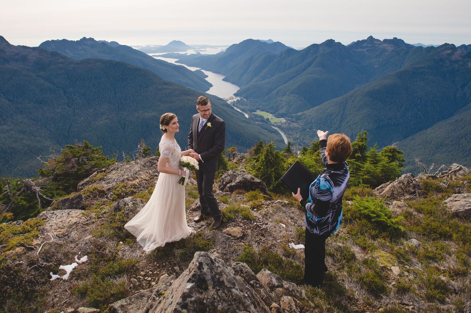 Wedding ceremony taking place on a scenic mountain summit with vast valley views.