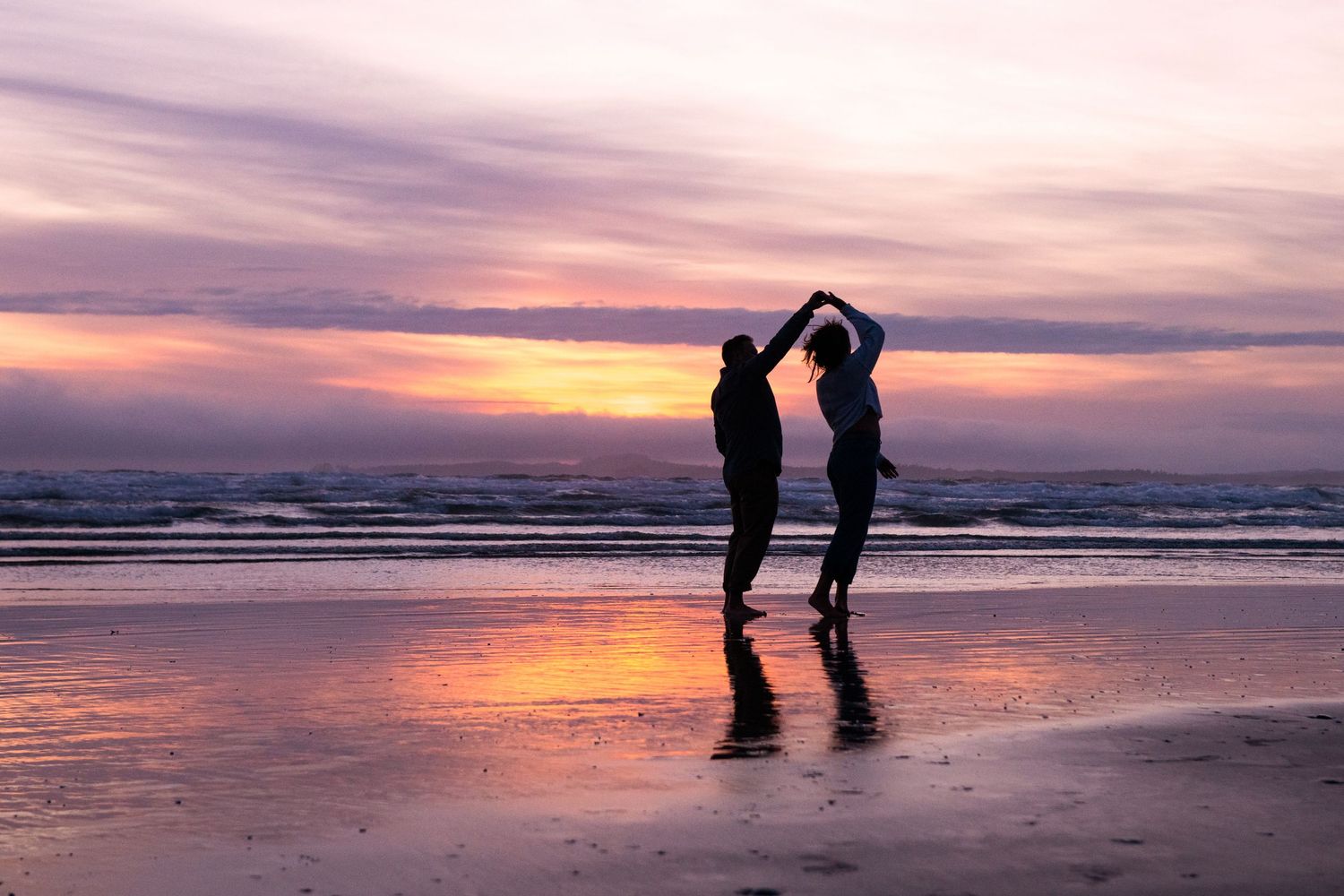 Silhouettes against a dramatic purple and orange sunset on a peaceful beach.