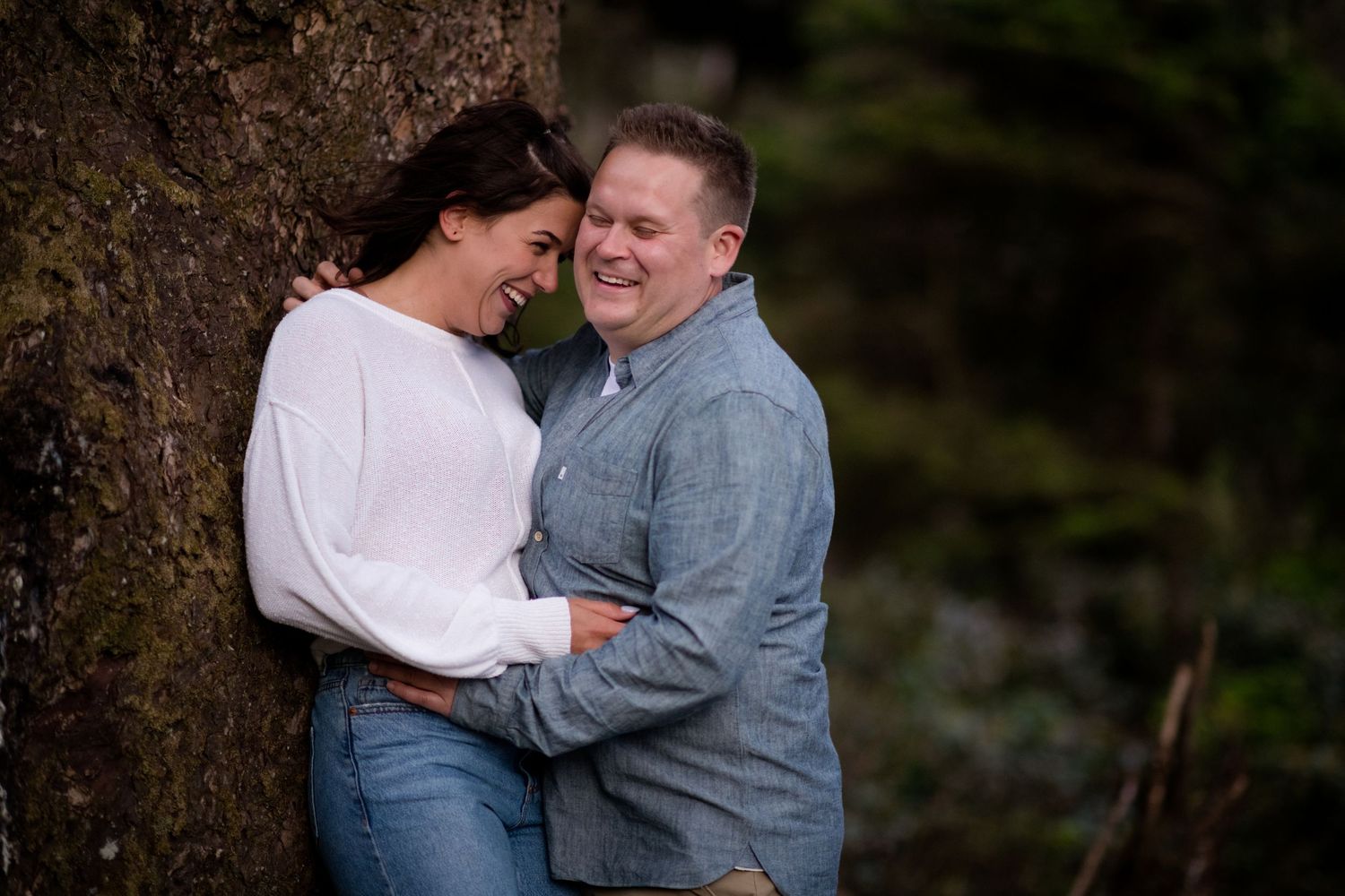A couple shares a joyful moment while embracing by a large tree.