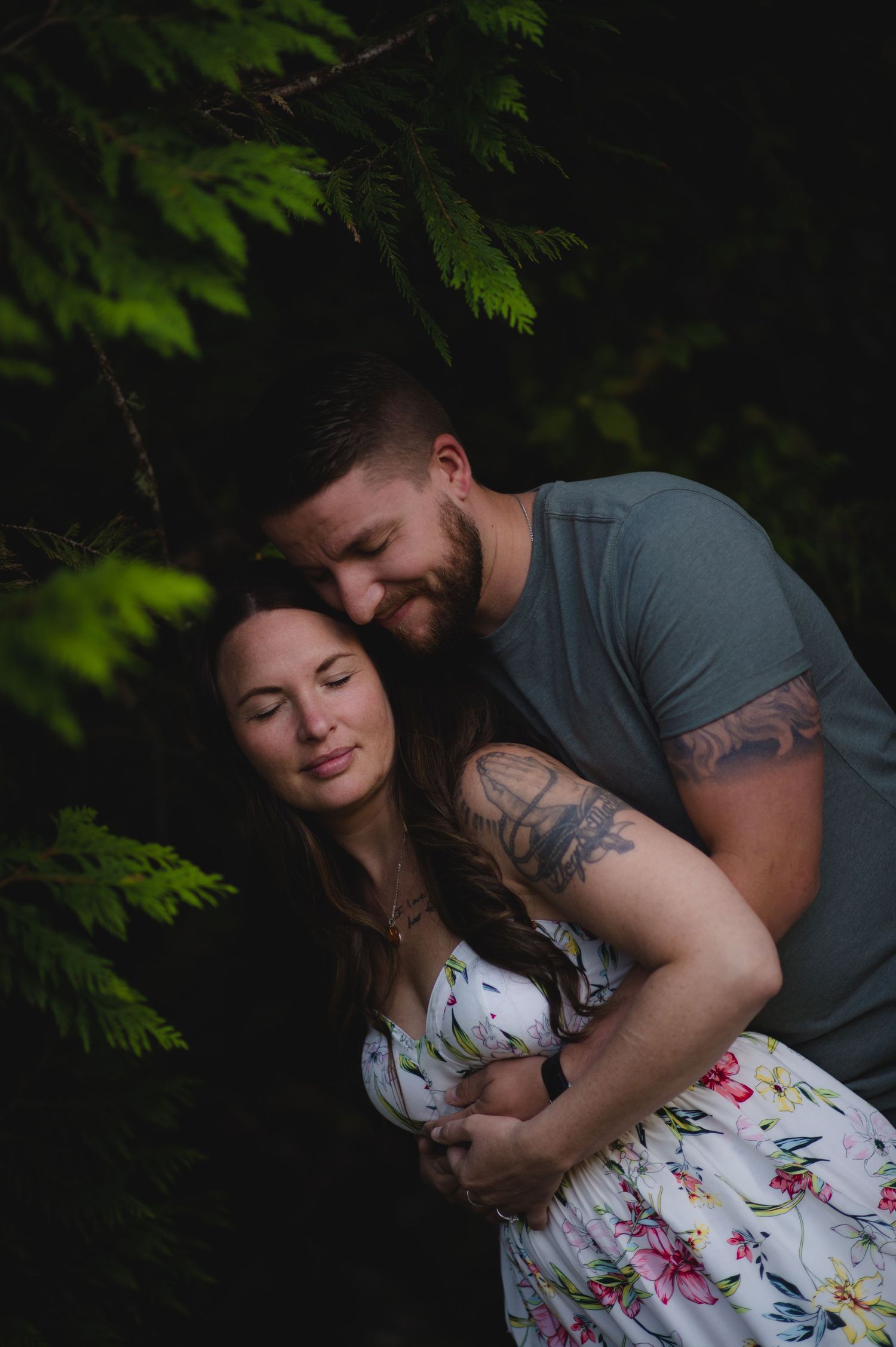 A tender embrace between a couple photographed in moody forest lighting.