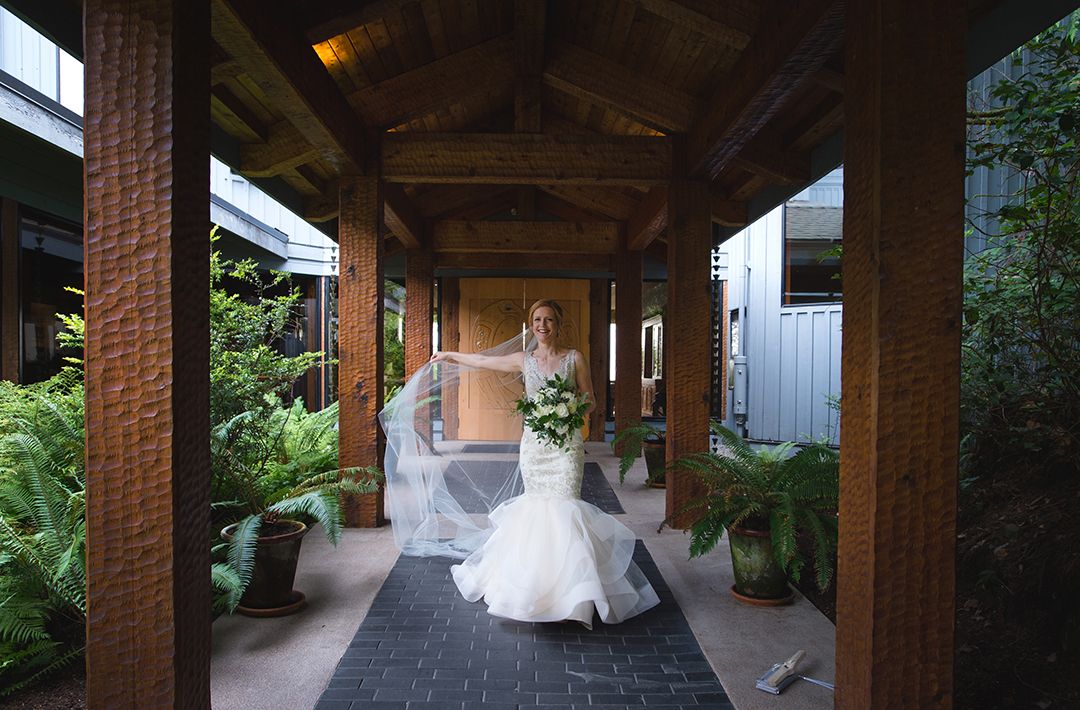Covered walkway with wooden beams and brick columns in garden setting.