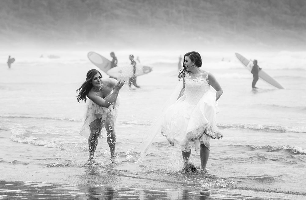 Playful wedding party splashing in ocean waves wearing formal attire.
