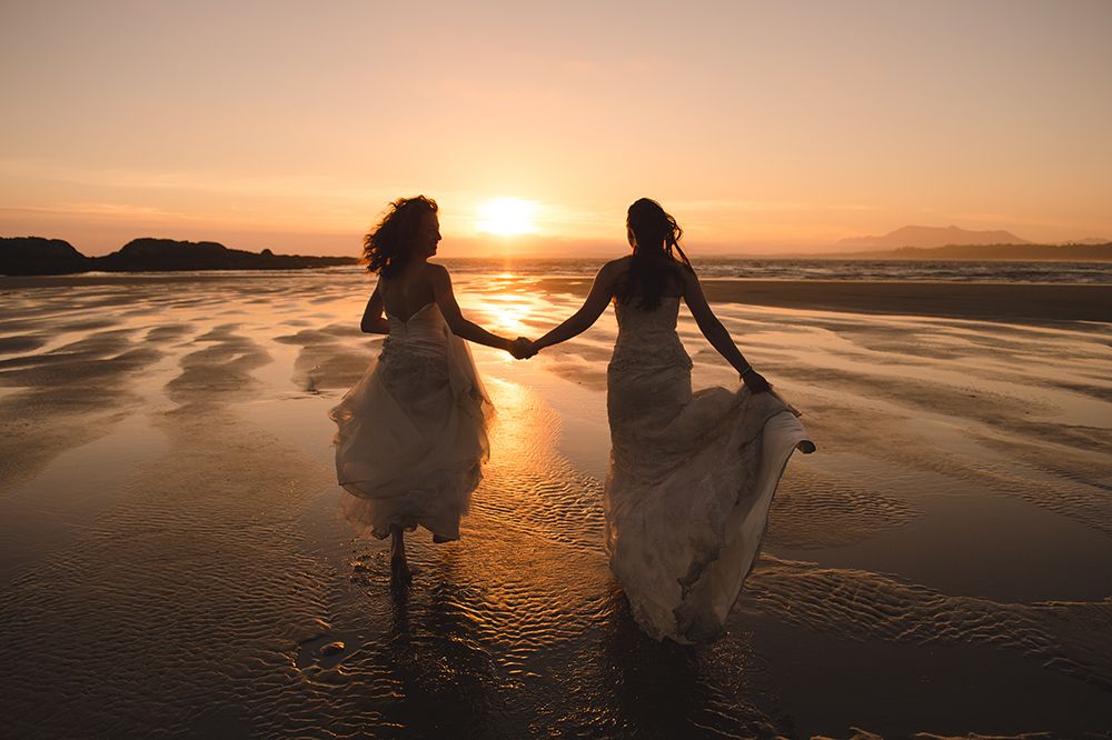 A couple walks hand in hand on a beach at sunset creating silhouettes against the golden sky.