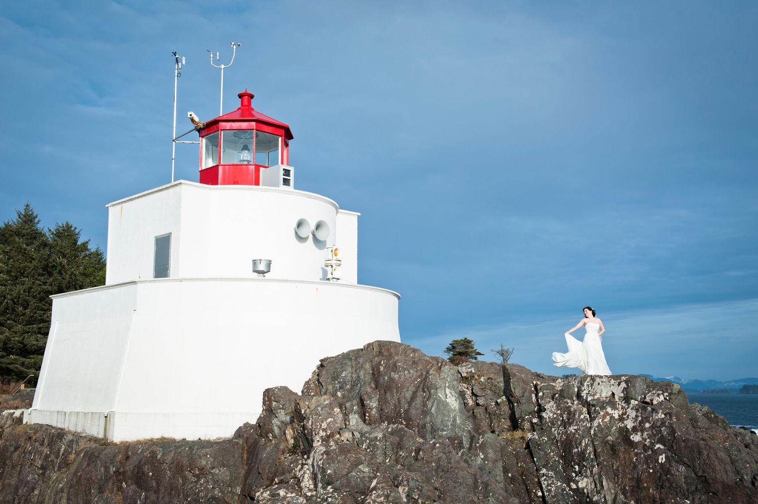 White lighthouse station perched on rugged coastal cliffs against blue sky.