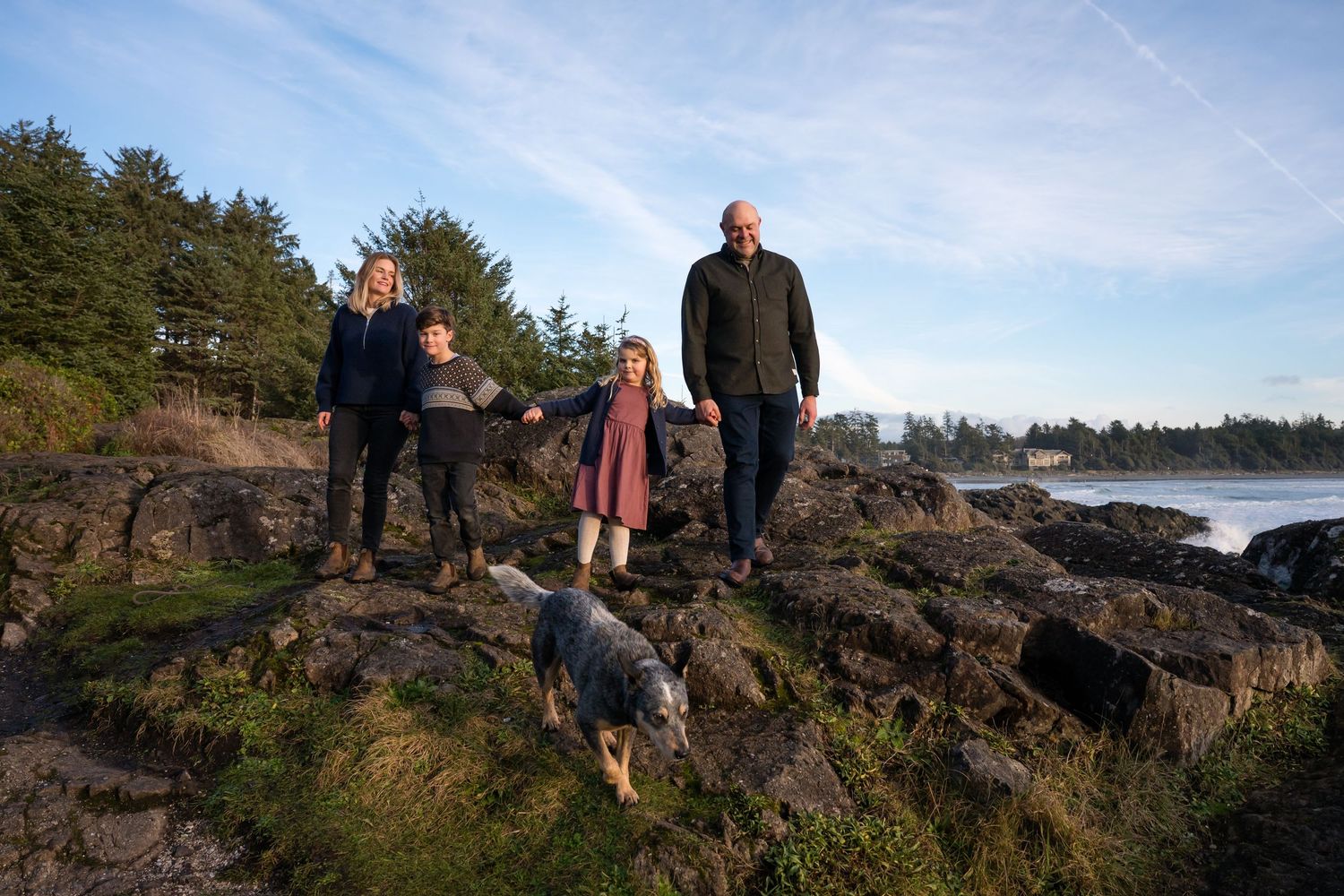 Two people stand together on rugged Pacific Northwest coastline under blue skies.