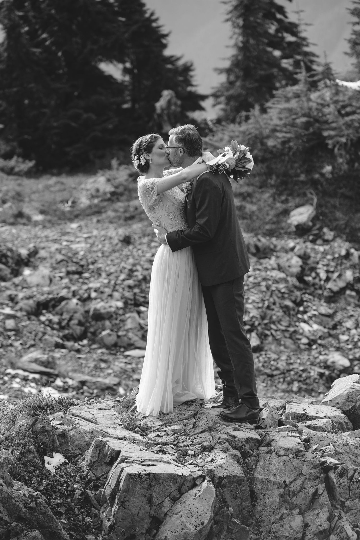 A romantic black and white wedding moment captured on a rocky mountain ledge.