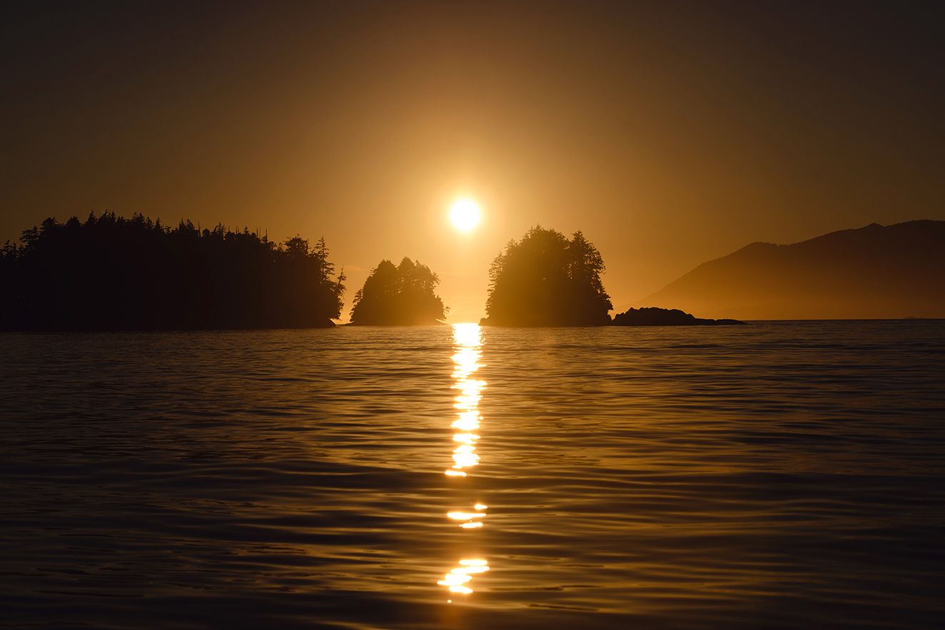 Dramatic sunset over calm ocean waters with silhouetted islands on the horizon.