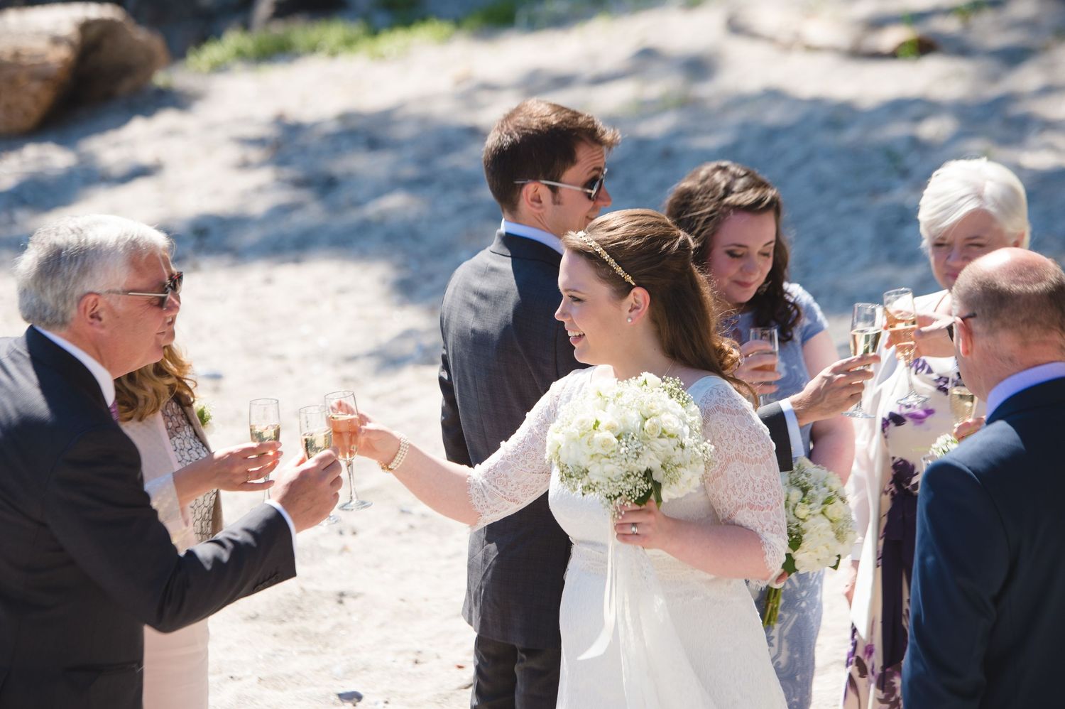 Wedding guests raising glasses in a celebratory toast outdoors.