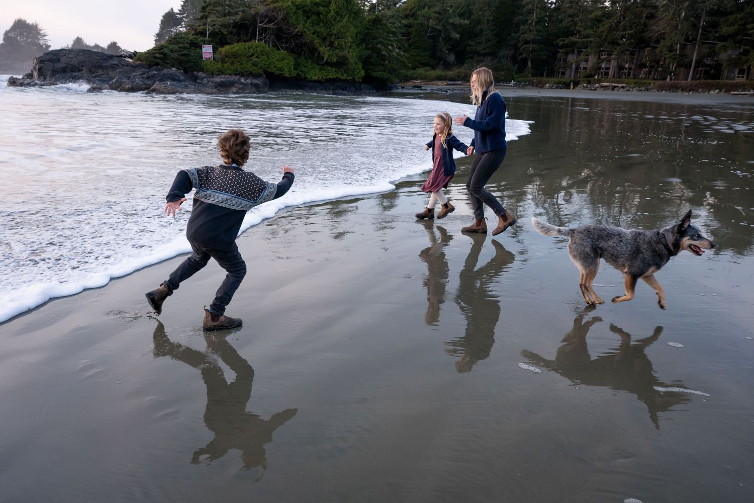 Beachgoers running and playing in wet sand with reflections visible.