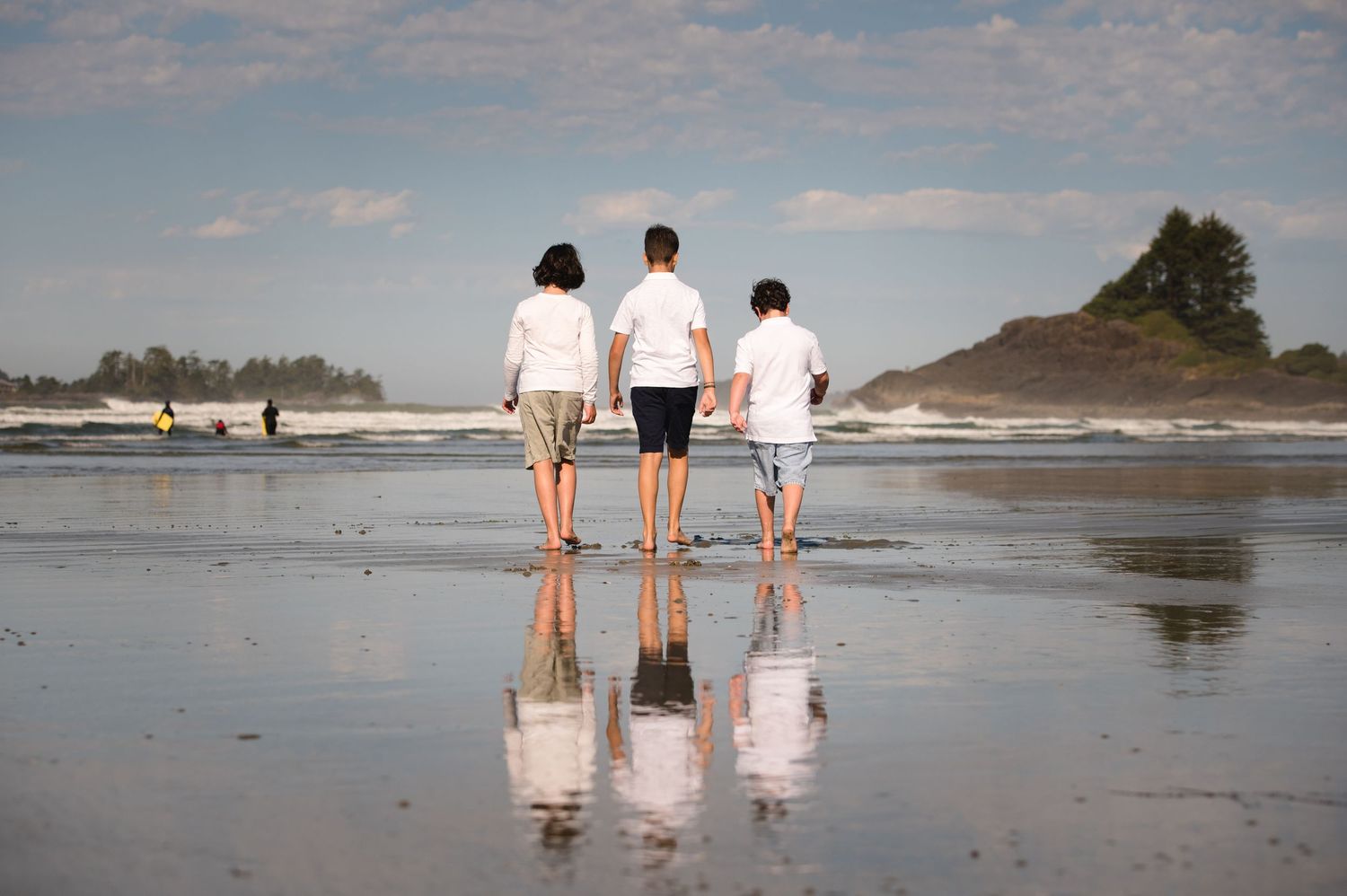 Three people walking on wet sand with their reflections visible beneath them.