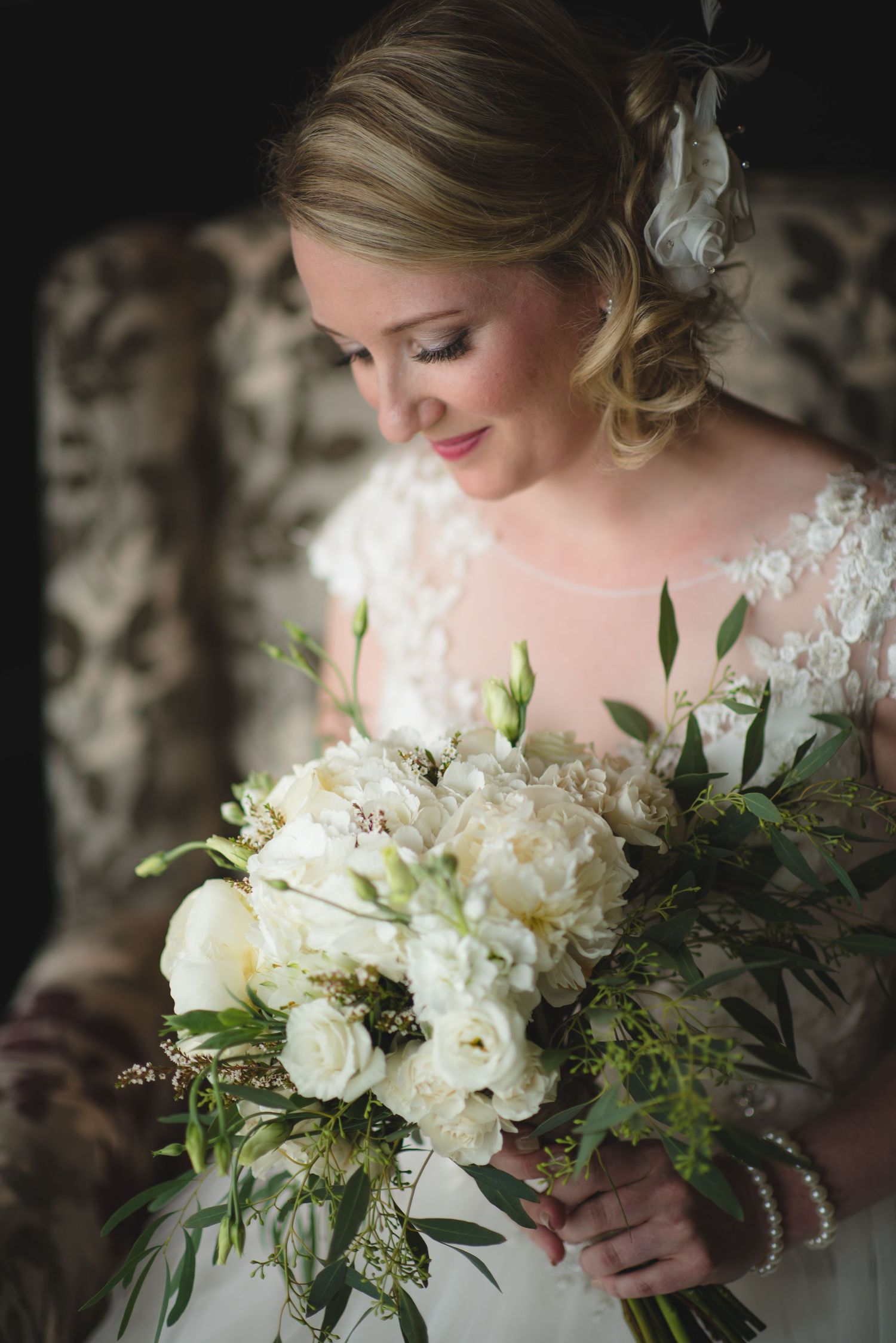 Elegant white bridal bouquet with roses and greenery against dark background.