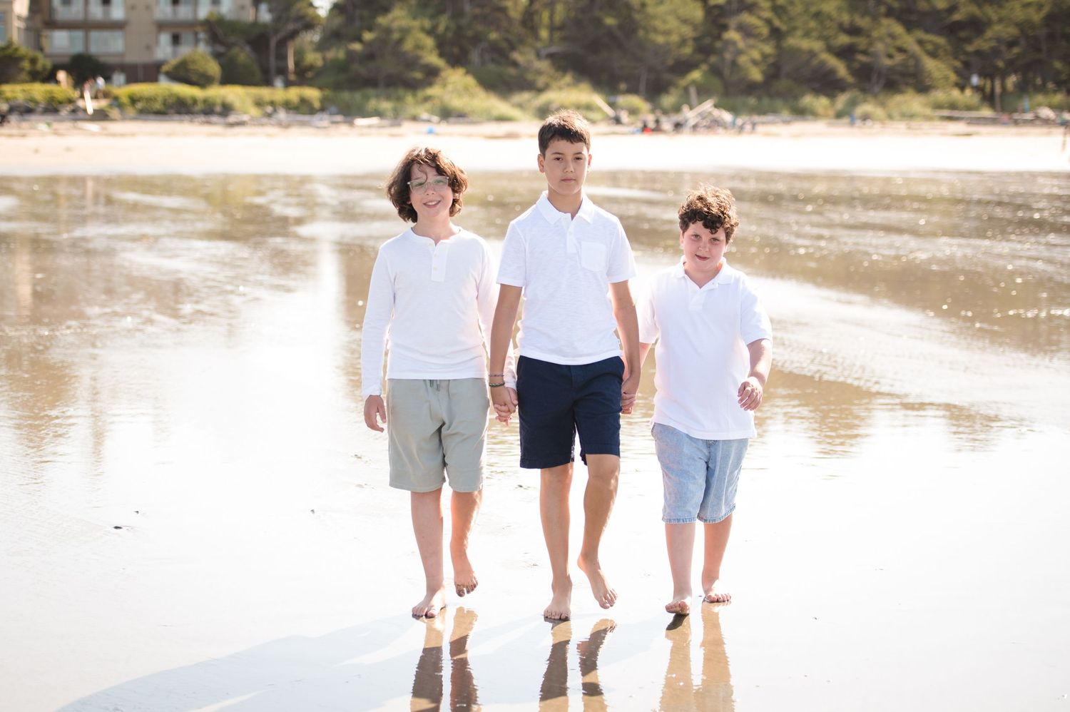Three people walking together on a reflective beach during sunset.