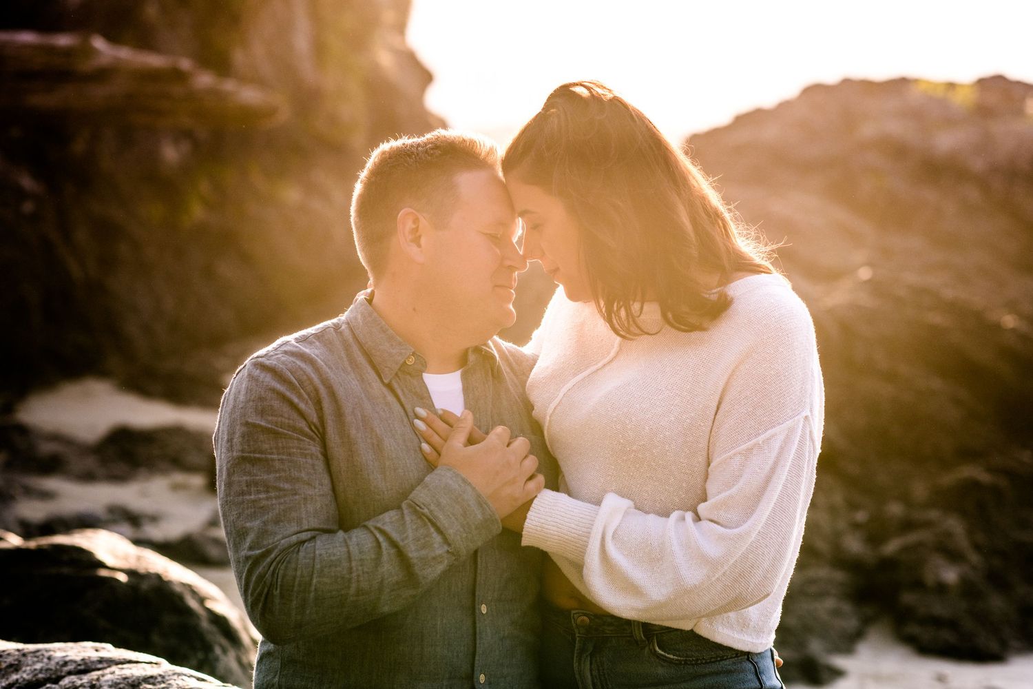 A couple shares an intimate moment on rocky coastal cliffs during golden hour.