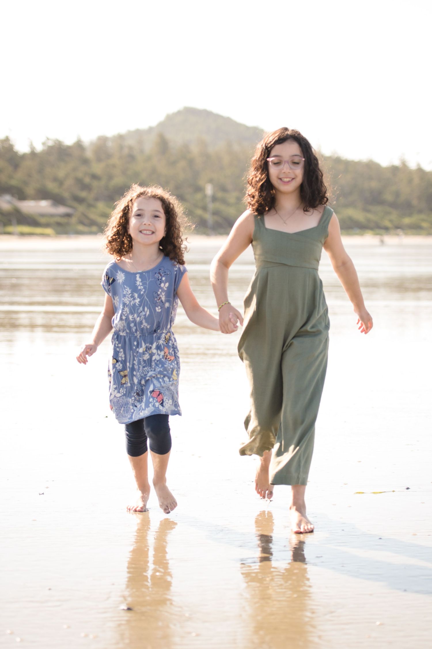 Two people running and playing together in shallow beach water during sunset.