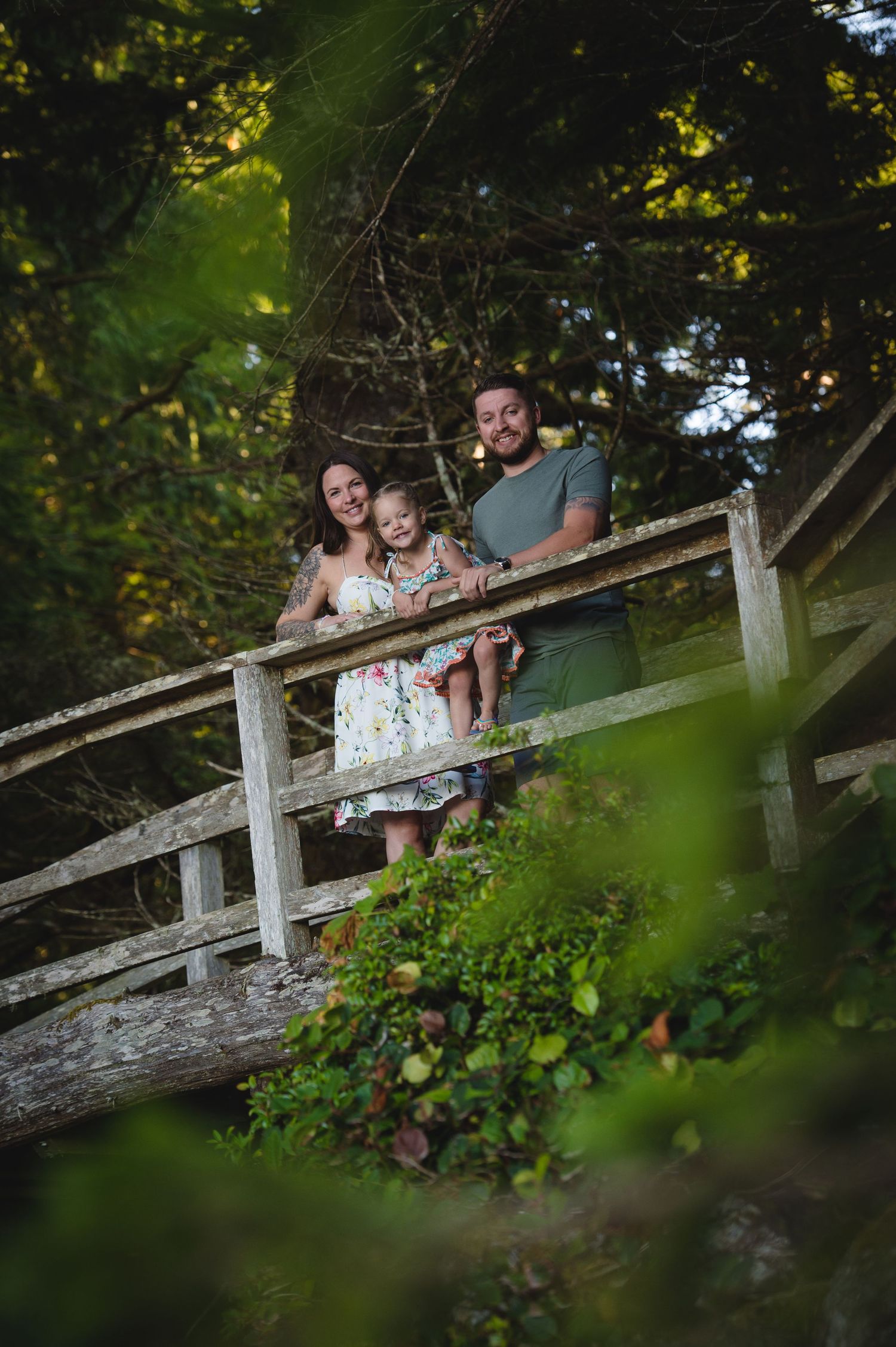 Family moment captured through leaves on weathered wooden bridge in forest setting.