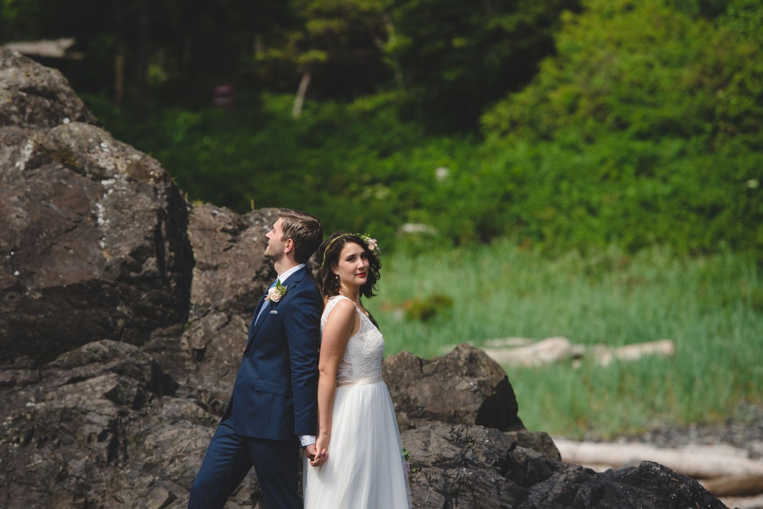 A couple poses playfully against dramatic coastal rocks near the ocean.