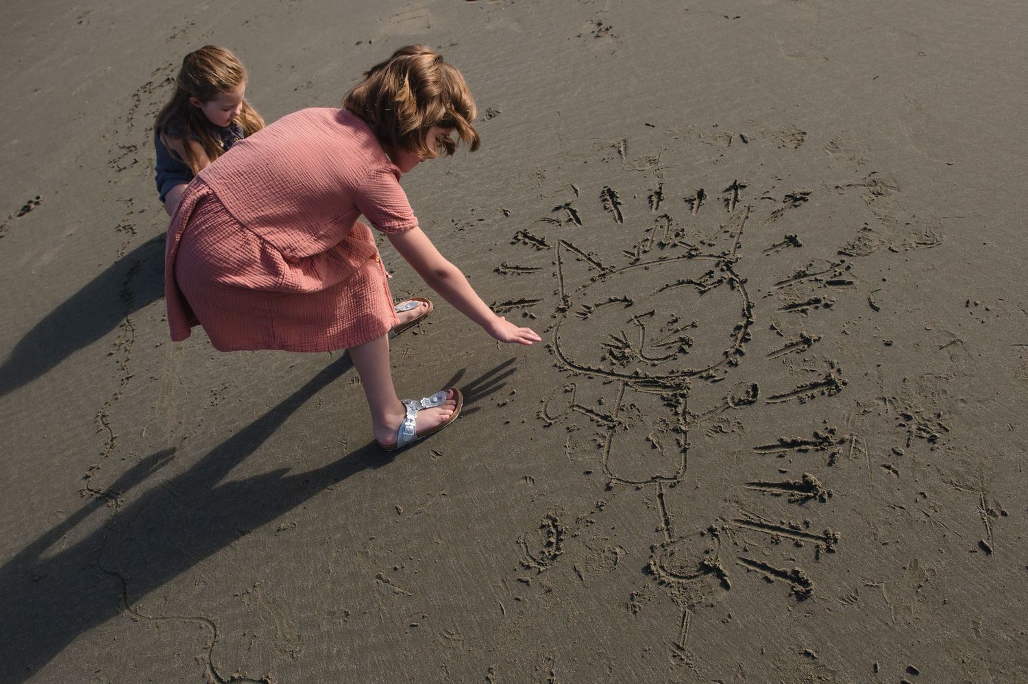People drawing patterns in the wet sand on a cloudy beach day.