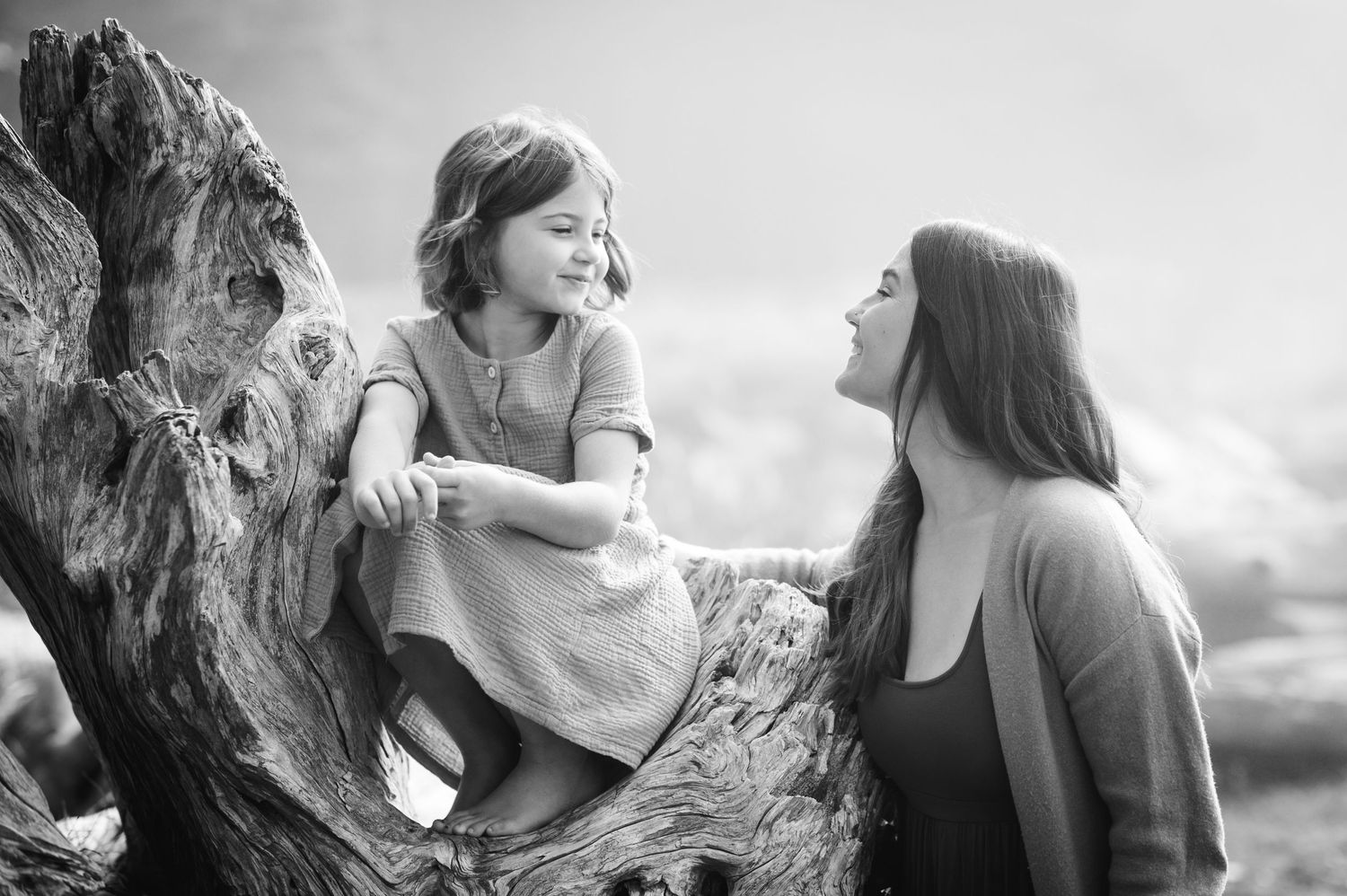 A candid black and white moment of joyful interaction on a weathered log outdoors.