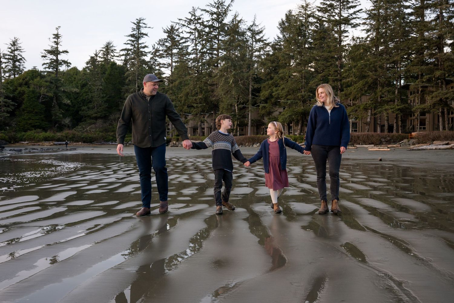 Wide angle view of a family exploring a rocky beach surrounded by tall evergreen trees.