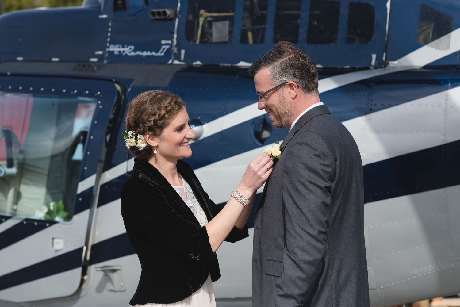 Couple shares intimate moment next to blue and white helicopters at an airfield.