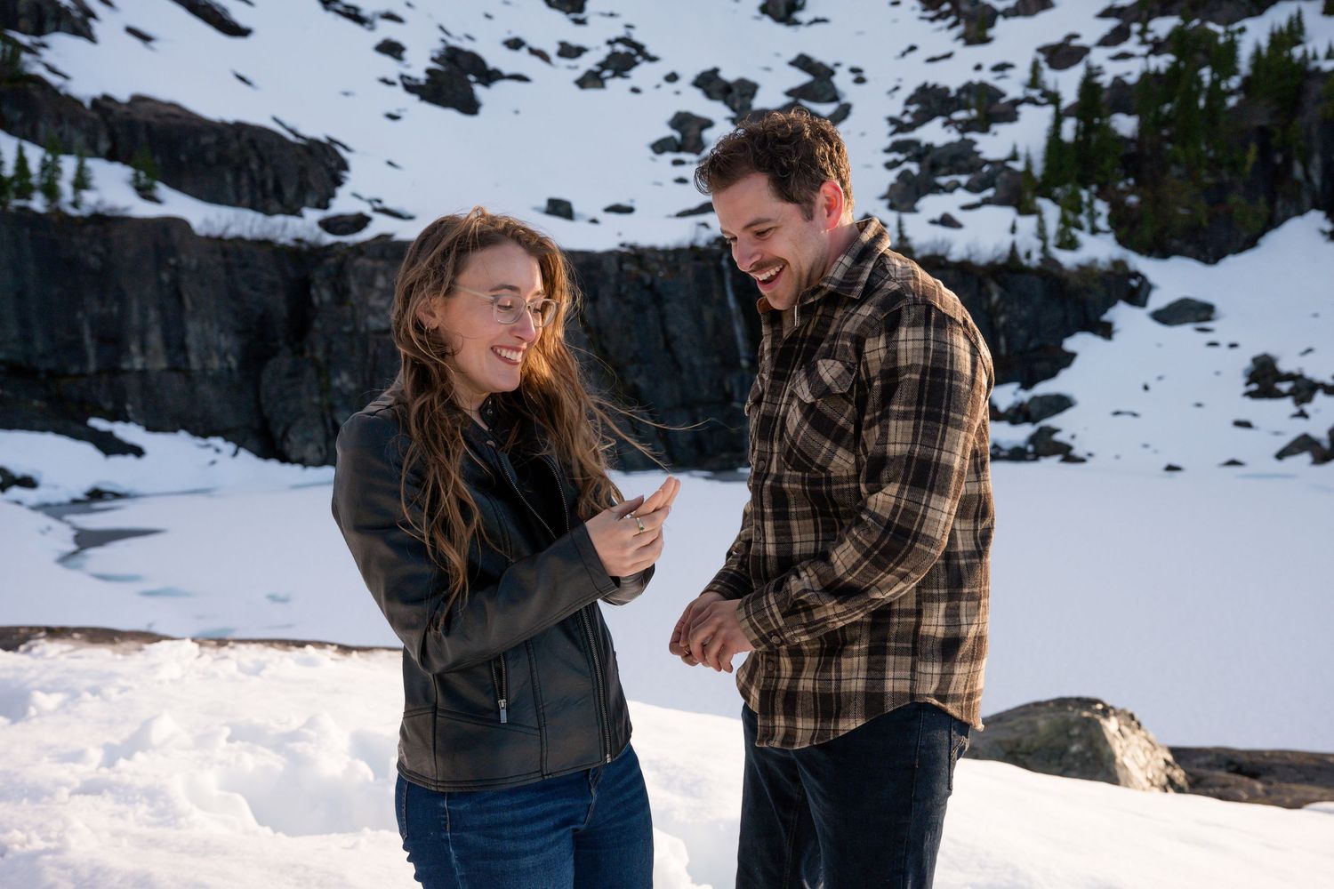 Couple laughing together in a snowy mountain landscape during winter engagement photos.