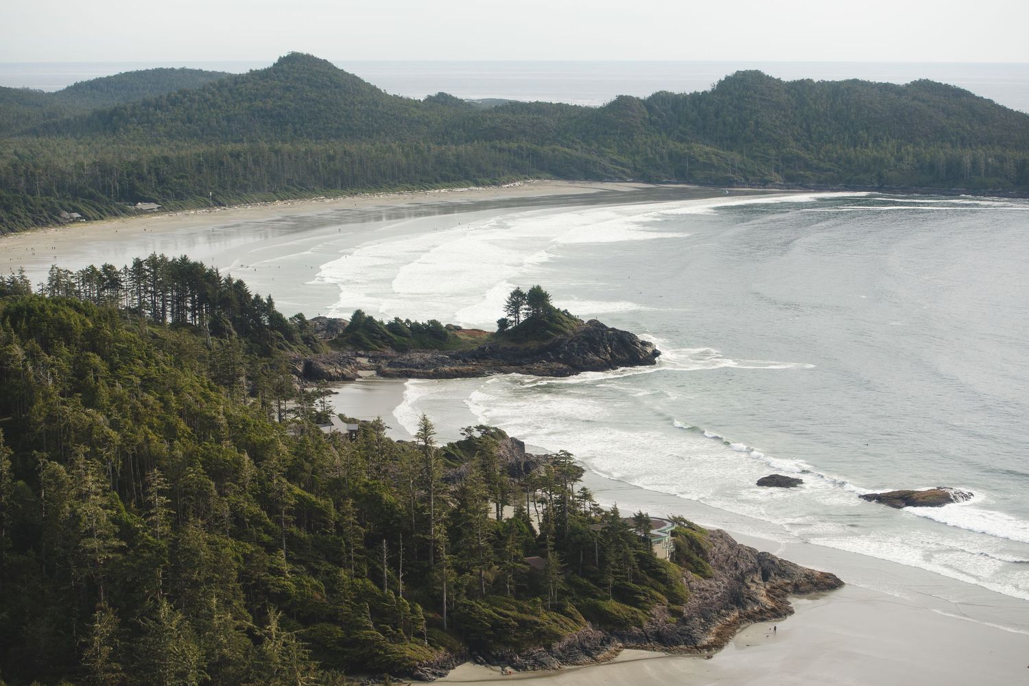 Aerial view of a scenic coastline with forested headlands and curved sandy beaches.