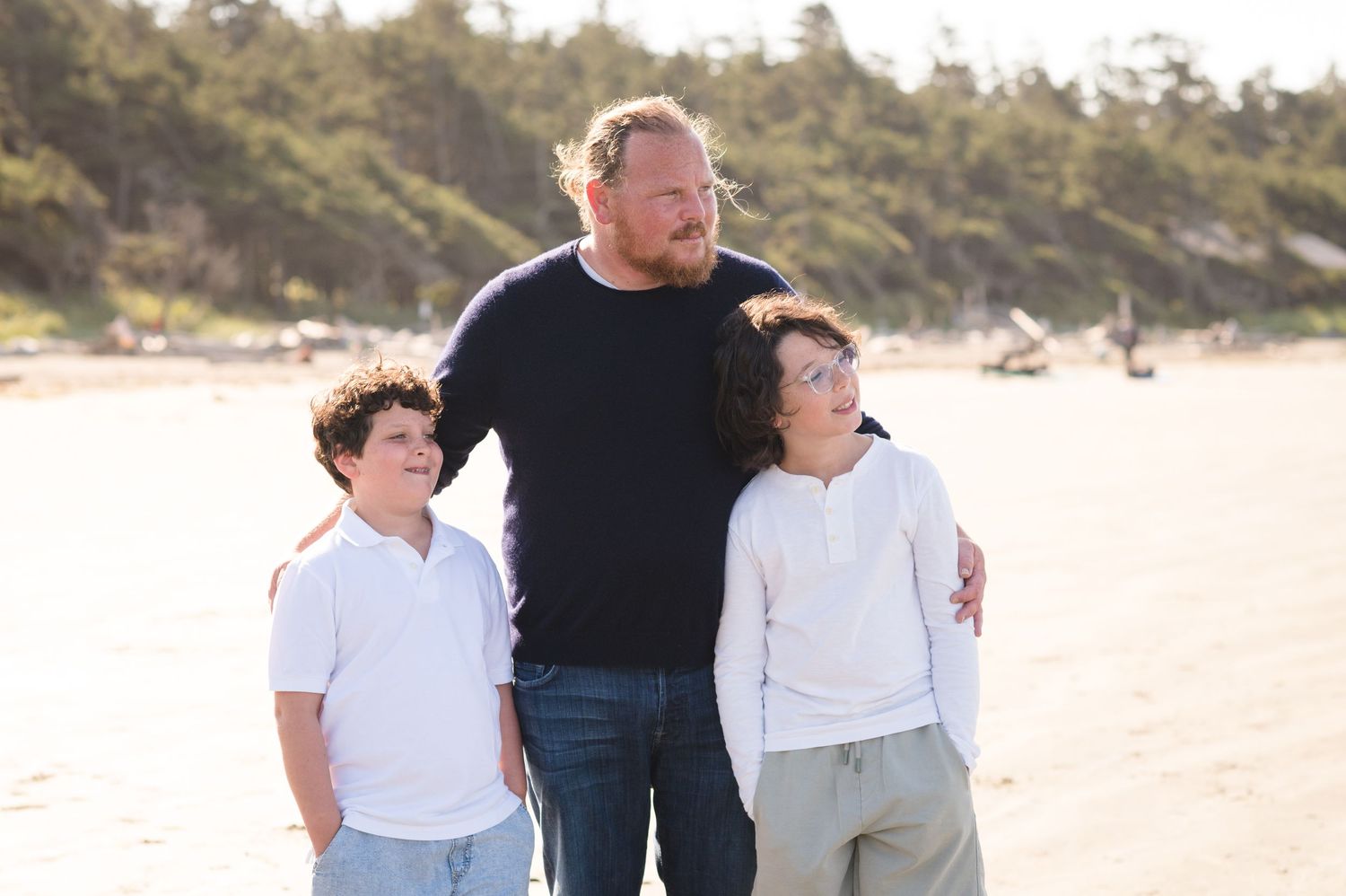 Family members embracing while walking on wet sand at the beach with hills in background.
