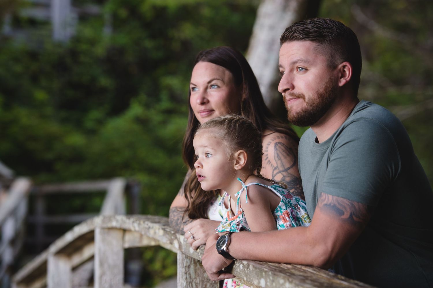 Family sharing a tender moment while sitting on rustic bridge railing in wooded setting.