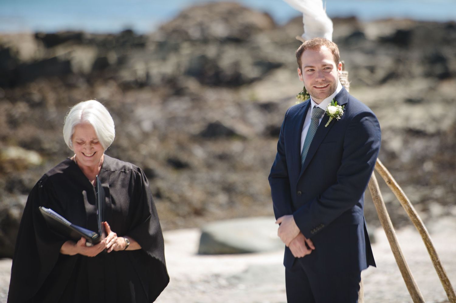 Wedding ceremony participants gathered on a rocky coastal beach.