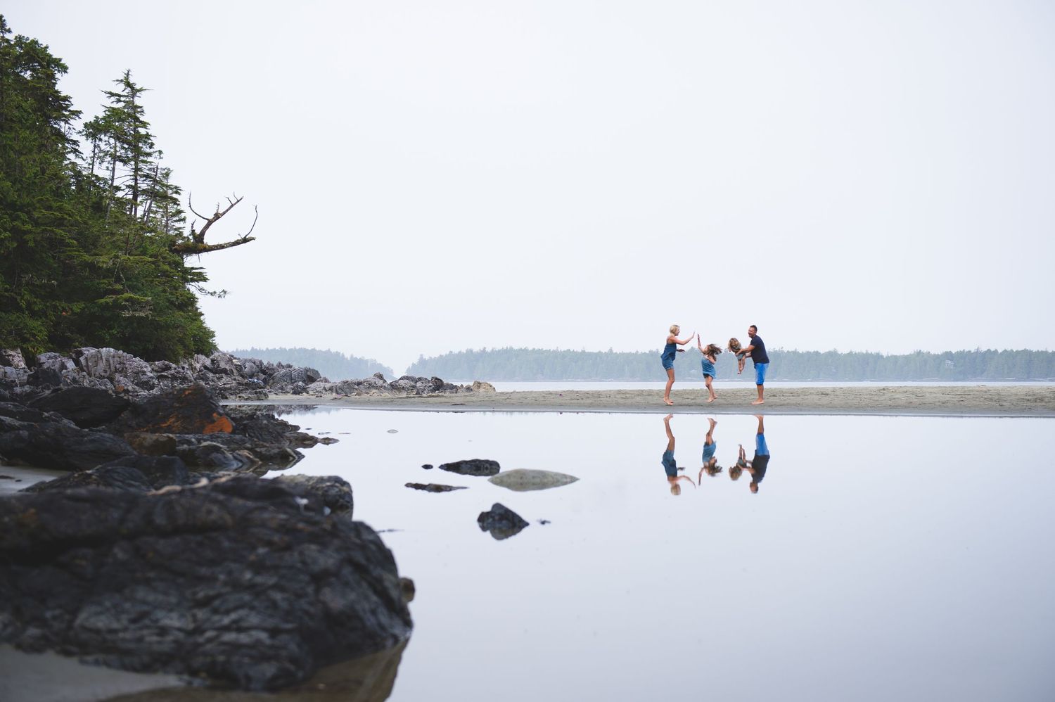 Group walking along rocky coastline with ocean and islands in background on overcast day.