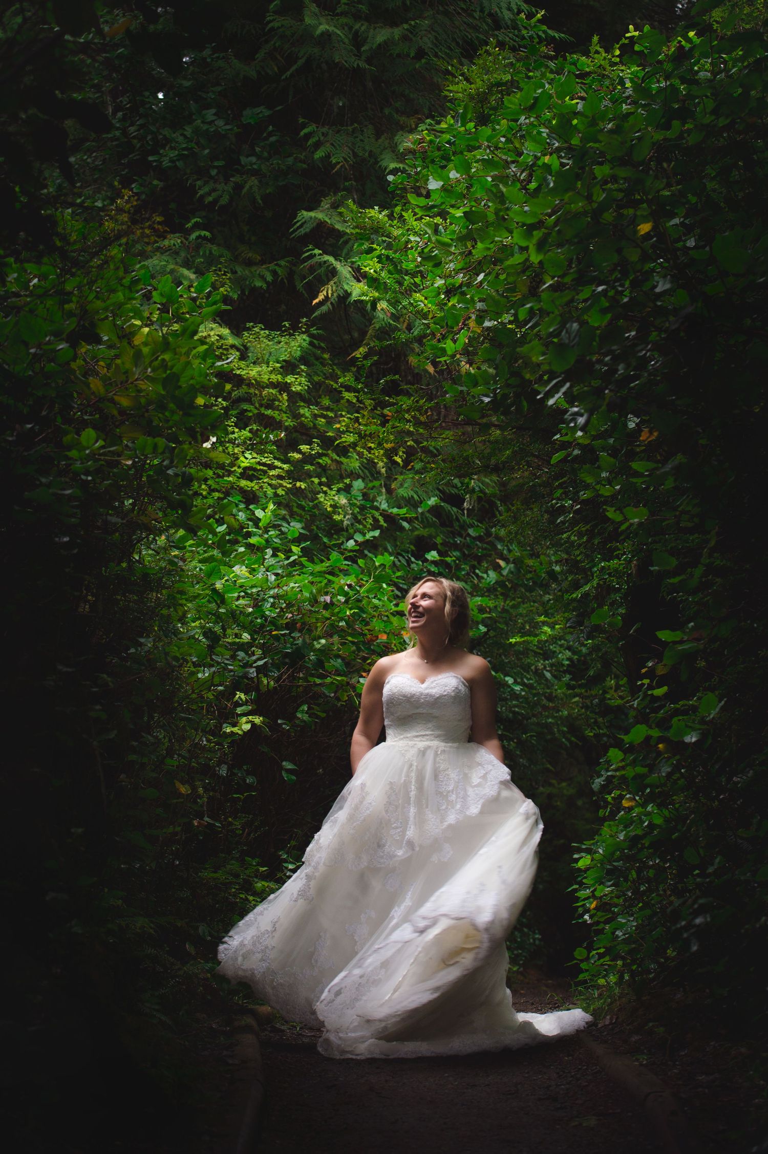 A bride in a flowing white gown twirls in a lush green forest setting.