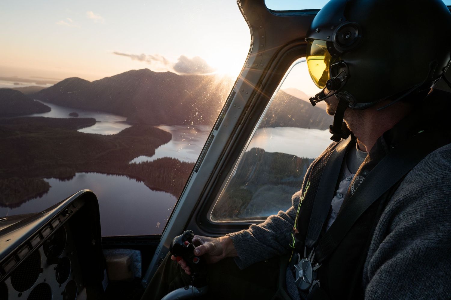 Tofino helicopter pilot with Atleo Air flying over stunning lake and mountain landscape during golden sunset aerial adventure.