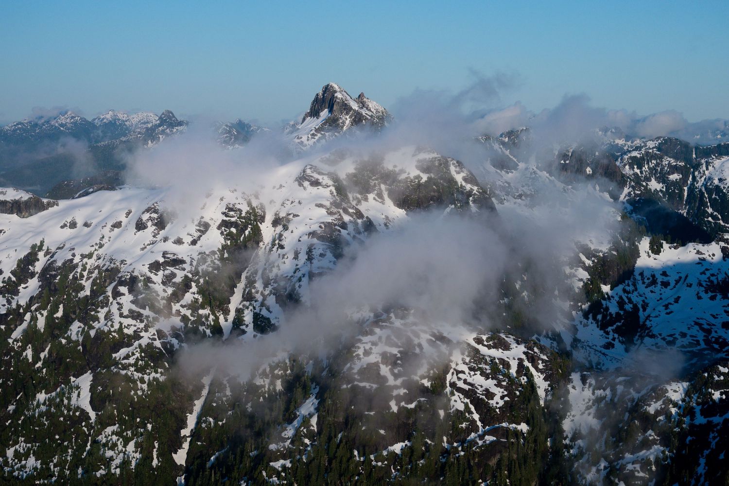Snow-capped mountain peaks emerge through wispy clouds in a stunning aerial winter landscape.