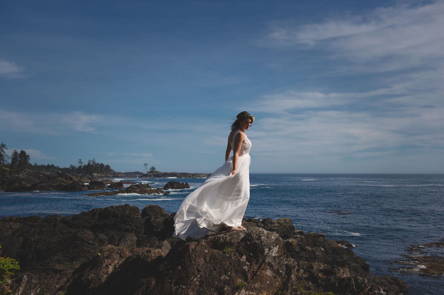 A flowing white dress moves in the wind on rocky ocean cliffs under blue skies.